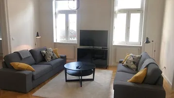 Helles Wohnzimmer mit zwei grauen Sofas, einem Couchtisch und Parkettboden, beleuchtet durch große Fenster.
