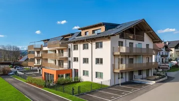 Modernes Mehrfamilienhaus mit mehreren Balkonen, Holzdetails und Außenparkplätzen unter blauem Himmel.