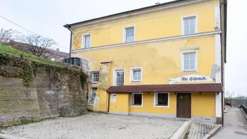 Gelbes historisches Gebäude mit gepflastertem Vorplatz und dem Schriftzug "Alte Schmiede".