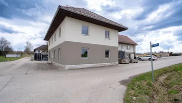 Mehrfamilienhaus mit zwei Stockwerken und Satteldach in ländlicher Umgebung.