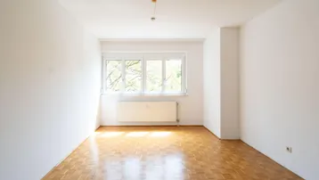 Helles, leeres Zimmer mit Parkettboden und großem Fenster, bereit zur individuellen Gestaltung.