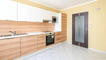 Moderne Küche mit hellen Holzfronten, weißen Oberschränken und integrierten Geräten auf gefliestem Boden.