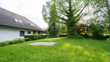 Großer Gartenbereich mit gepflegtem Rasen, hohen Bäumen und einem Teil des Hauses.