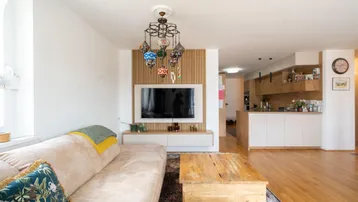 Heller offener Wohnbereich mit beigem Sofa, Holztisch und integrierter moderner Küche im Hintergrund.
