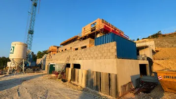Baustelle eines neuen Gebäudes mit Kran und Baumaterialien unter blauem Himmel.