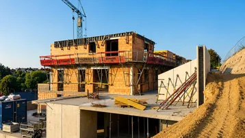 Baustelle eines neuen Gebäudes mit Kran und Rohbau unter blauem Himmel.