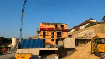Baustelle eines neuen Gebäudes mit Kran, Bagger und Baucontainern unter blauem Himmel.