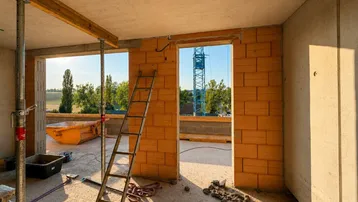 Unfertiger Innenraum eines Neubaus mit Ziegelwänden und Blick auf die Baustelle.
