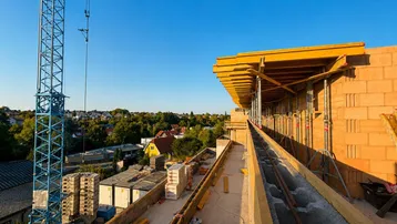 Baustelle eines Neubaus mit Kran und Blick auf die umliegende Wohngegend unter blauem Himmel.