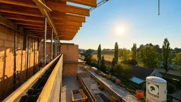 Baustelle eines Neubaus bei Sonnenuntergang mit Blick auf die umliegende Landschaft und Felder.