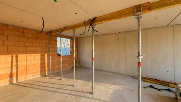 Innenraum eines Rohbaus mit Ziegelwänden und Deckenstützen, bereit für den weiteren Ausbau.