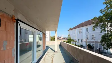 Balkon im Rohbau mit Blick auf die Nachbargebäude und den blauen Himmel.