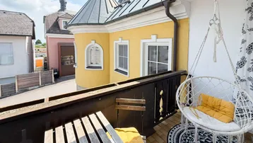Gemütlicher Balkon mit Hängesessel und Blick auf ein charmantes gelbes Gebäude mit Turm.