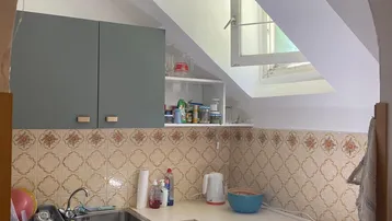 Kleine Küche mit Dachschräge, Einbauschränken, Herd und Spüle, beleuchtet durch ein Dachfenster.