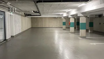 Geräumige Tiefgarage mit Betonwänden, sichtbaren Rohren und markierten Parkplätzen.