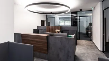 Moderner Empfangsbereich in einem Bürogebäude mit stilvollen Arbeitsplätzen und Glastüren.