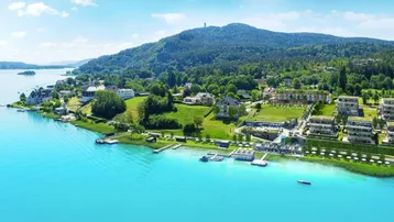 Panoramablick auf eine luxuriöse Wohnanlage am Seeufer mit Bergen und üppiger Vegetation im Hintergrund.