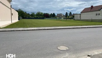 Großes, unbebautes Grundstück mit Rasenfläche und angrenzender Straße unter bewölktem Himmel.