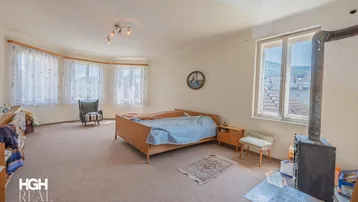 Helles Schlafzimmer mit Teppichboden, Holzofen und weitem Ausblick über die Dächer.