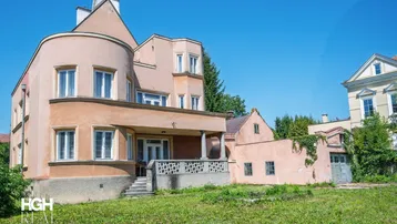 Historisches Gebäude mit markanter Architektur und großem Gartenbereich unter blauem Himmel.