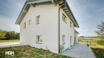 Seitenansicht des Neubaus mit kleiner gepflasterter Terrasse und Blick ins Grüne.