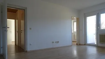 Helles, leeres Wohnzimmer mit Parkettboden und Zugang zu weiteren Räumen.