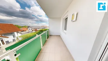 Langer Balkon mit Fliesenboden und Blick auf die umliegende Wohnsiedlung und grüne Landschaft.