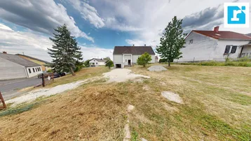 Weitläufiges Grundstück mit Einfamilienhaus, Zufahrt und umliegender Natur unter bewölktem Himmel.