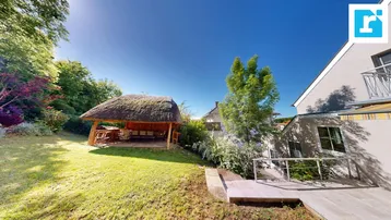 Sonnige Gartenanlage mit traditionellem Strohdach-Pavillon und Blick auf das Haus.