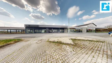 Modernes Geschäftsgebäude mit großem Parkplatz und weitem Himmel unter bewölktem Himmel.