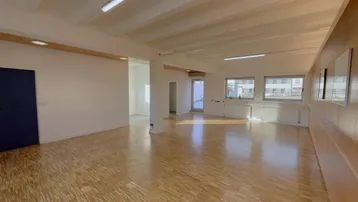 Geräumiger, heller Gewerberaum mit Parkettboden und großen Fenstern, ideal für verschiedene Nutzungen.