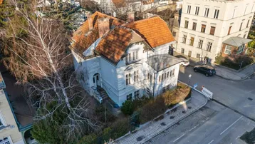 Luftaufnahme des historischen Gebäudes mit Ziegeldach und der umliegenden städtischen Bebauung.