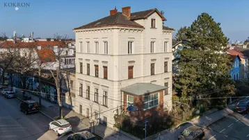 Luftaufnahme des historischen Gebäudes mit umliegender Straße und Bäumen bei sonnigem Wetter.