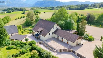 Luftaufnahme des Anwesens mit Haupthaus, Nebengebäude, Reitplatz und weitläufiger grüner Landschaft mit Bergen.