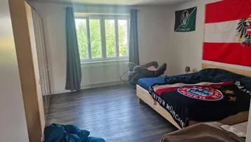 Helles Schlafzimmer mit großem Fenster, dunklem Laminatboden und einem geräumigen Kleiderschrank.