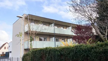 Modernes Mehrfamilienhaus mit mehreren Balkonen und gepflegter Hecke im Vordergrund.