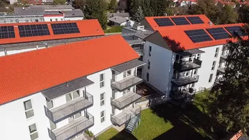 Luftaufnahme von modernen Wohngebäuden mit roten Dächern und Photovoltaikanlagen.