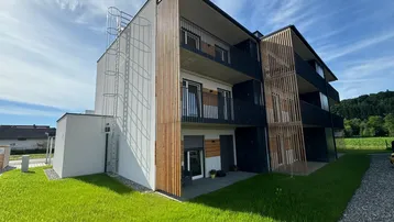 Modernes Mehrfamilienhaus mit Holzverkleidung und Balkonen unter blauem Himmel.