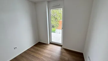 Helles Schlafzimmer mit Laminatboden und Zugang zu einem französischen Balkon.