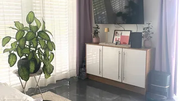 Helles Wohnzimmer mit großformatigen Fliesen, einem Fernseher an der Wand und bodentiefen Fenstern.
