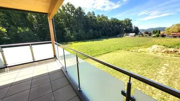 Überdachter Balkon mit Fliesenboden, Glasgeländer und weitem Blick ins Grüne.