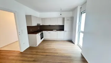 Leere Küche mit Einbauküche, Laminatboden und Zugang zu einem Fenster.