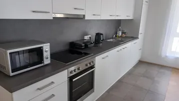 Moderne Küche mit weißen Schränken, dunkler Arbeitsplatte und integrierten Geräten.