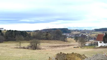 Weitläufige Landschaft mit Feldern und vereinzelten Häusern unter einem bewölkten Himmel.