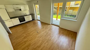 Heller Wohn- und Küchenbereich mit Laminatboden, weißen Schränken und direktem Zugang zur Terrasse.