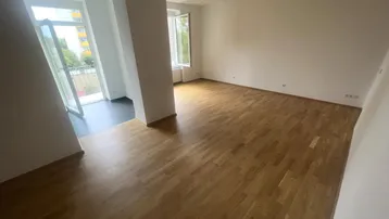 Helles Wohnzimmer mit Parkettboden und Zugang zu einem kleinen Balkon.