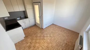 Helle Kochnische mit hellen Schränken, dunkler Arbeitsplatte und Parkettboden in einem Wohnraum.