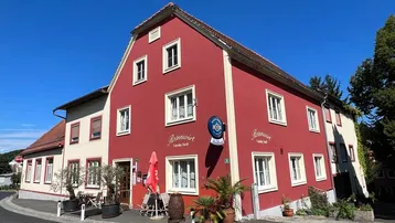 Rotes Gebäude mit weißen Fenstern und einem Schild "Rosenwirt" an einer Straßenecke.