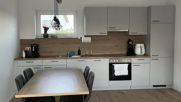 Moderne Küche mit grauen Schränken, Holzakzenten und einem Esstisch für gemeinsame Mahlzeiten.