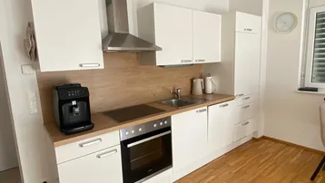 Moderne Einbauküche mit weißen Schränken, Holzarbeitsplatte und integrierten Geräten.
